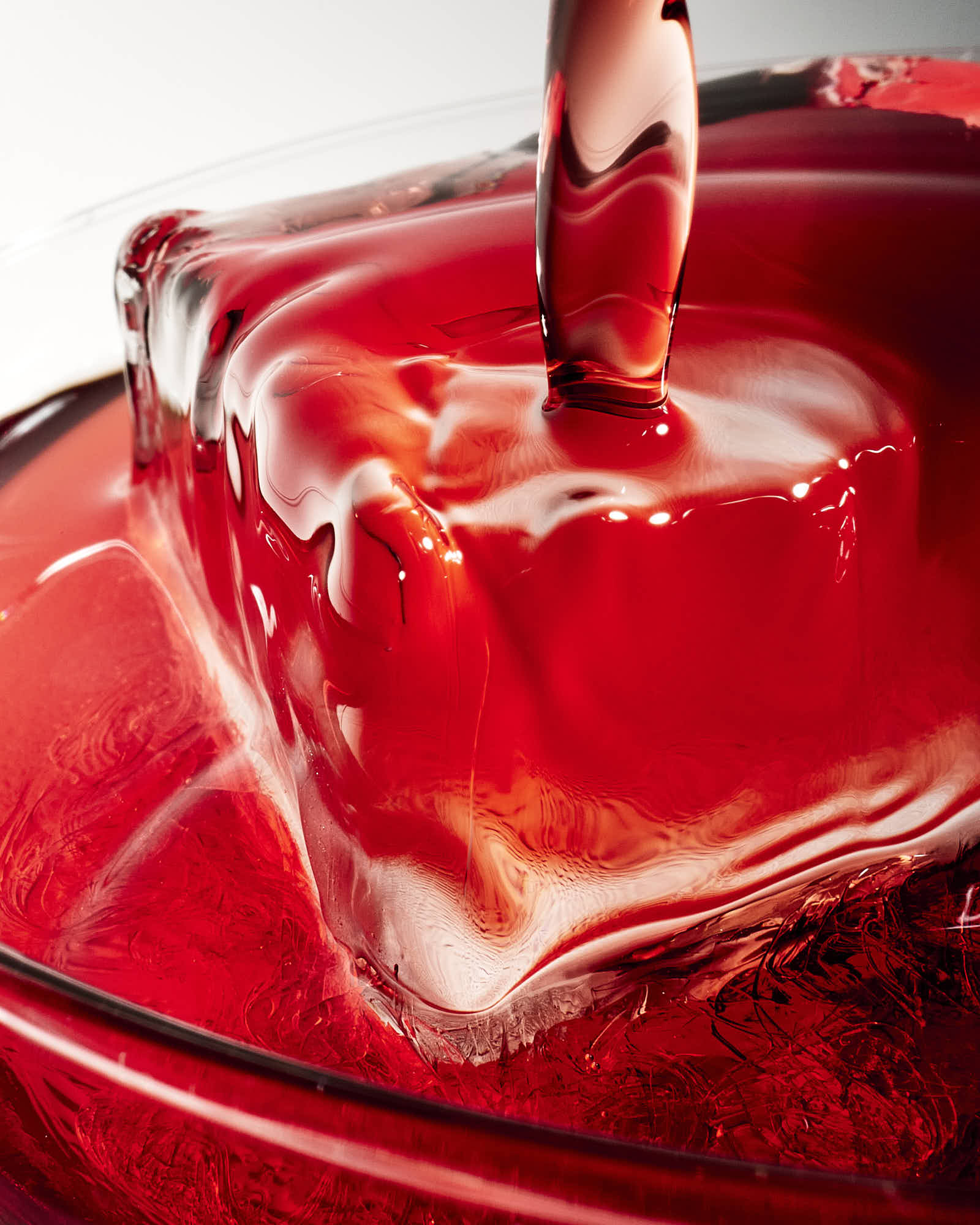 A close-up of red liquid being poured into a clear container, creating ripples and reflections.