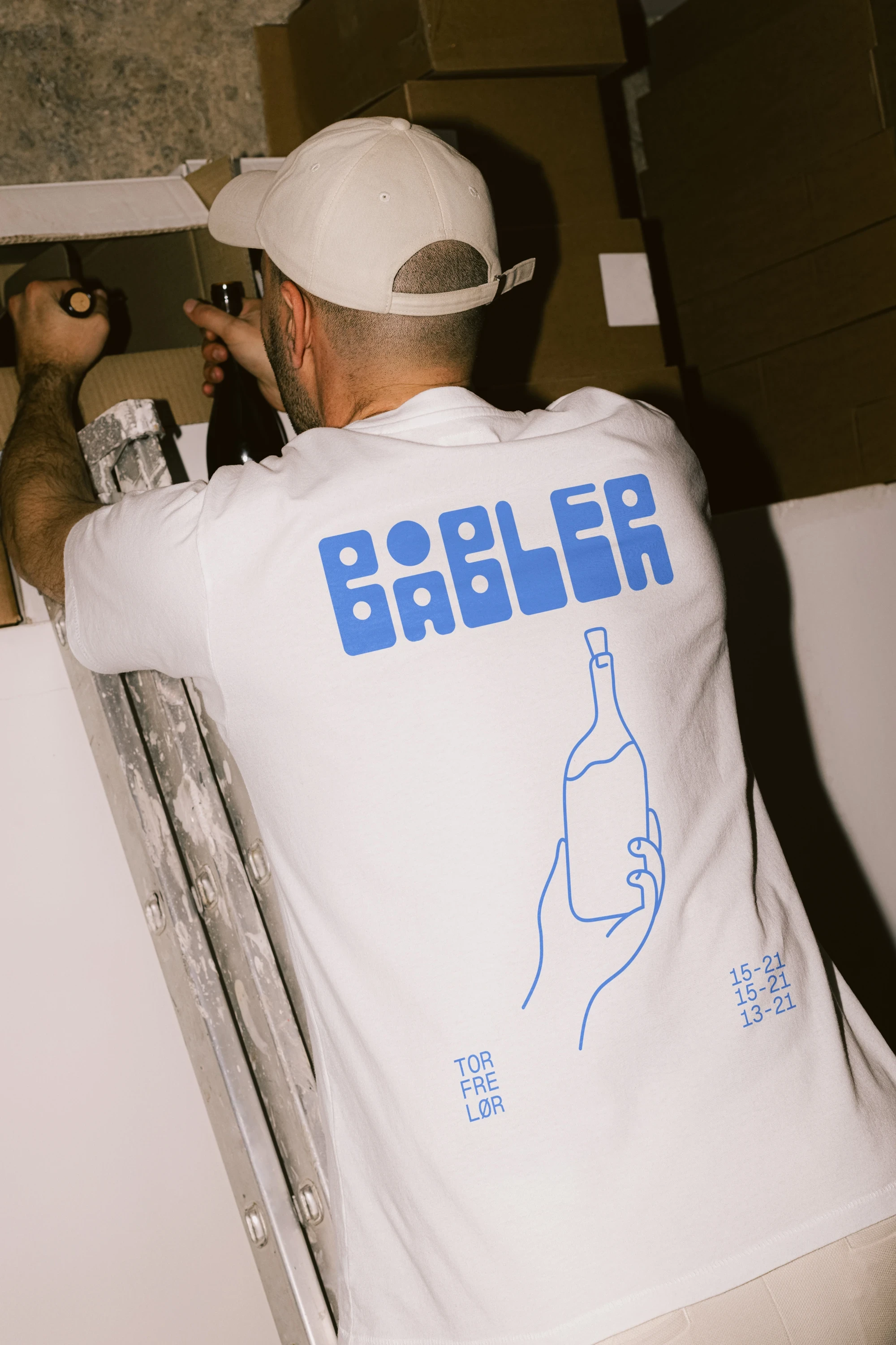 Bar worker collecting wines from the shelf, wearing the t-shirt designed for Båbler wine bar.