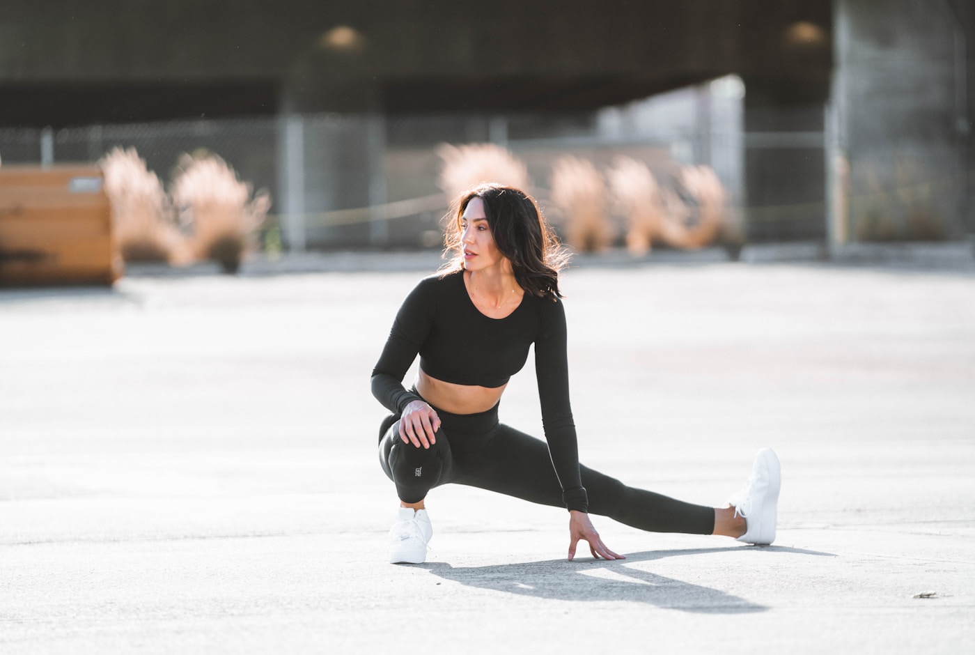 A woman in athletic wear performing a low lunge stretch outdoors before training