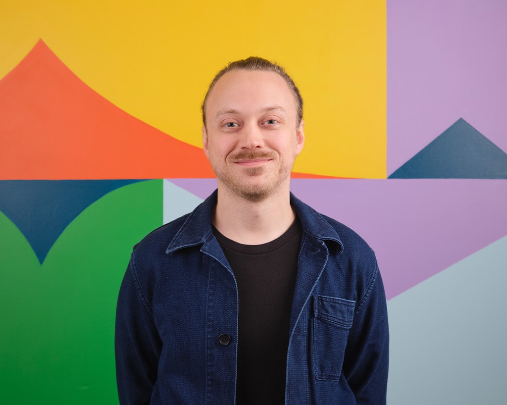 Portrait of Tristan Marantos standing in front of a colourful mural