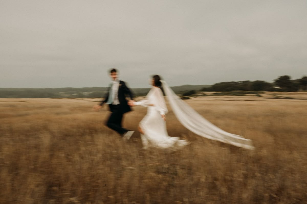 Bride and groom running through an open field during golden hour