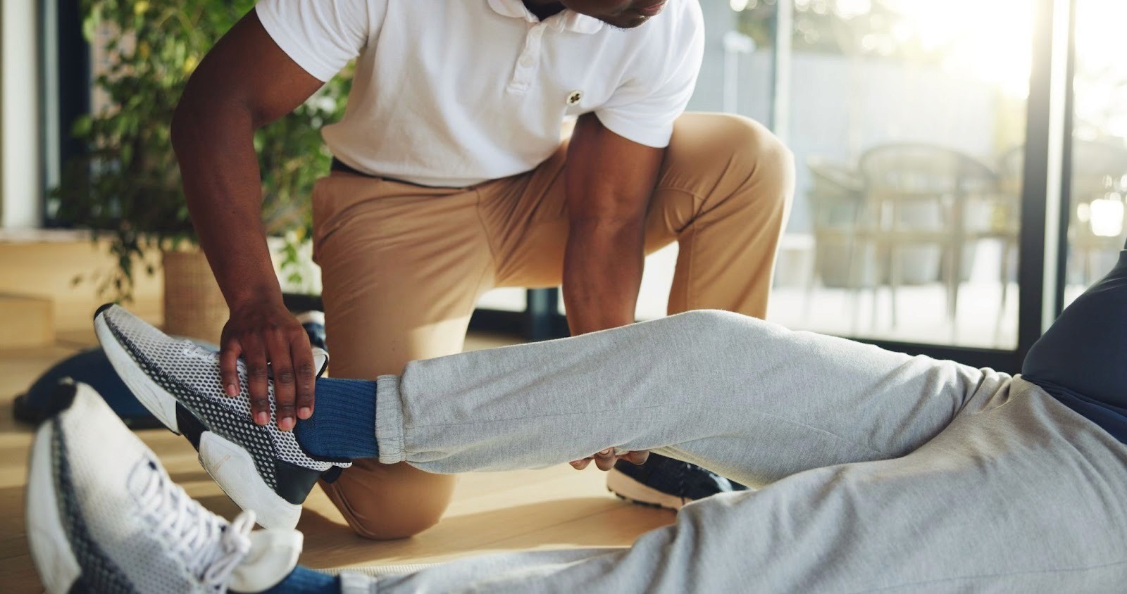 A physical therapist kneeling on a floor while stretching a patient's leg.