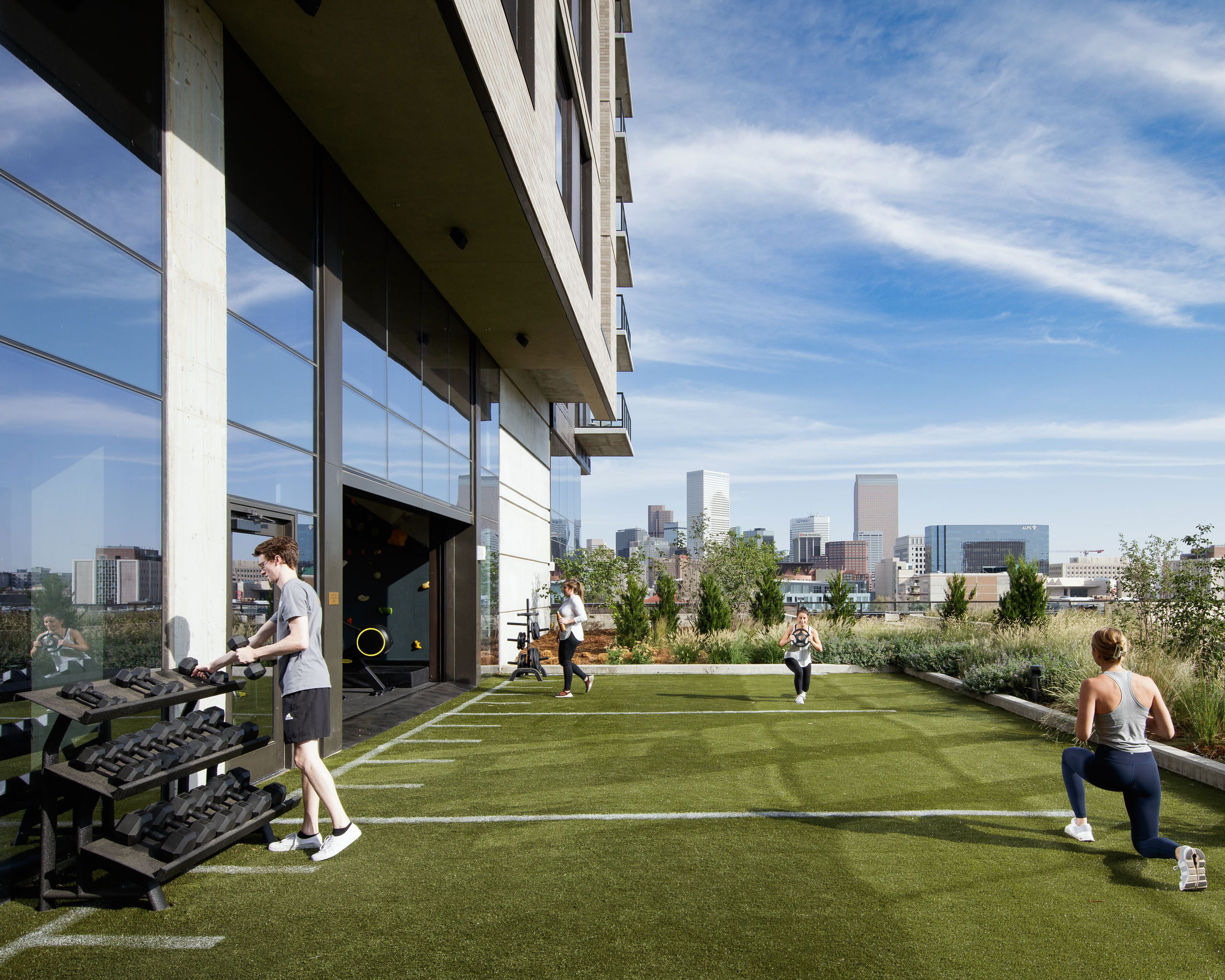 People exercising on an outdoor rooftop gym with city skyline view.