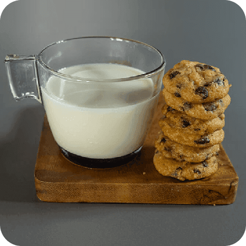Galletas con chispas de chocolate junto a un vaso de leche, en una escena cálida y casera.