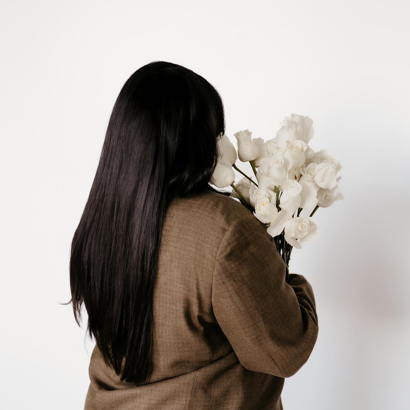 Woman holding white bouquet of roses with her back turned to the camera.