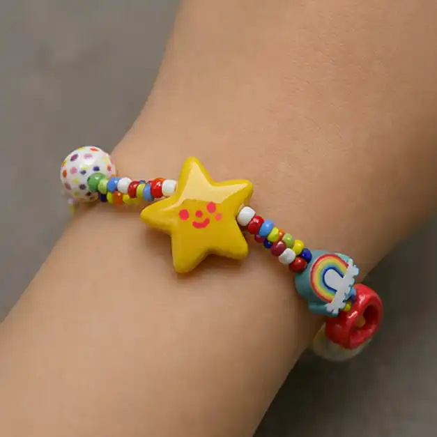 Et fargerikt perlearmbånd på et håndledd, med en stor gul stjerne med et smilefjes, en regnbue-perle og flerfargede småperler.