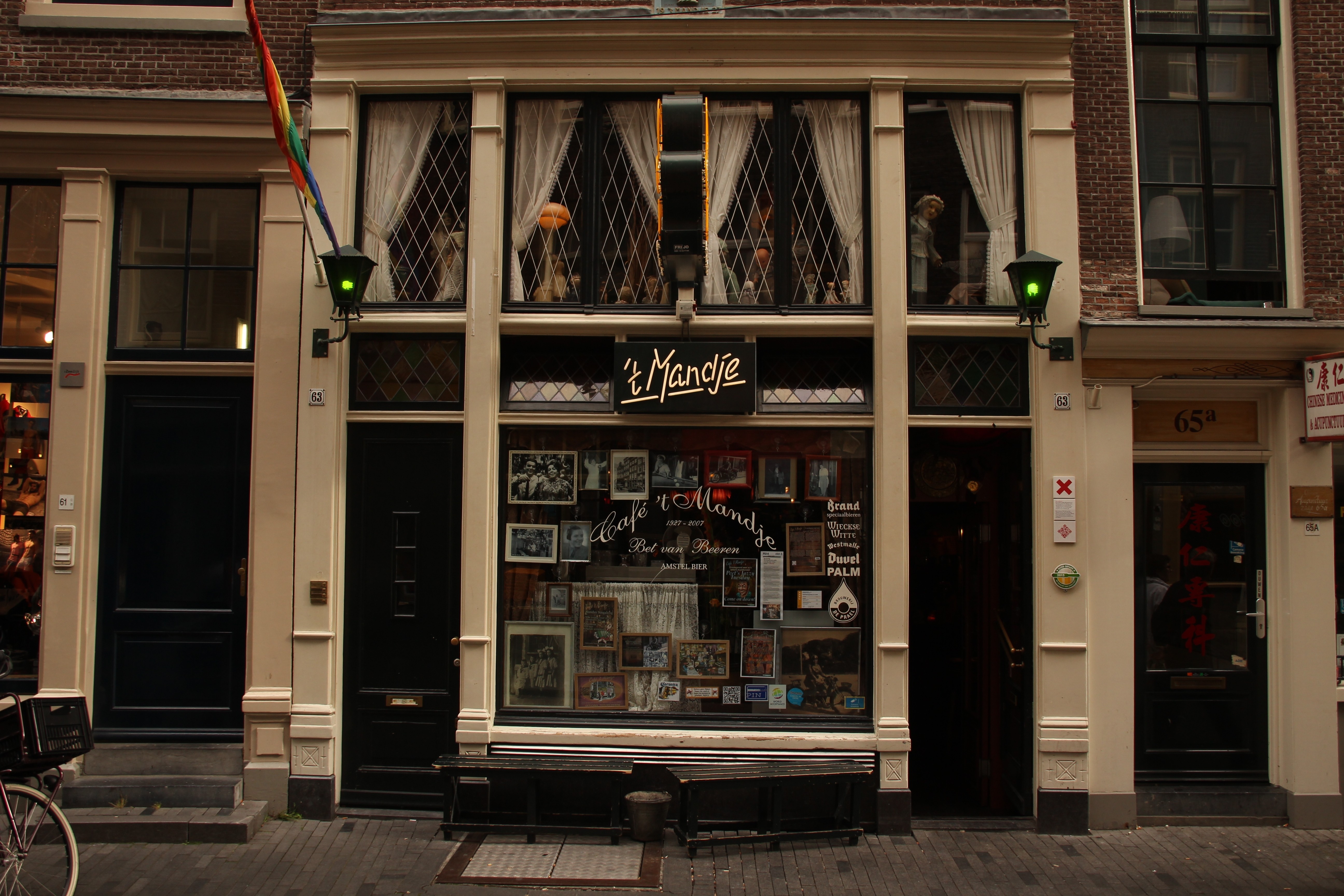 Cafe 't Mandje as viewed from the street, with a Pride flag marking the doorway and historic photographs visible inside.