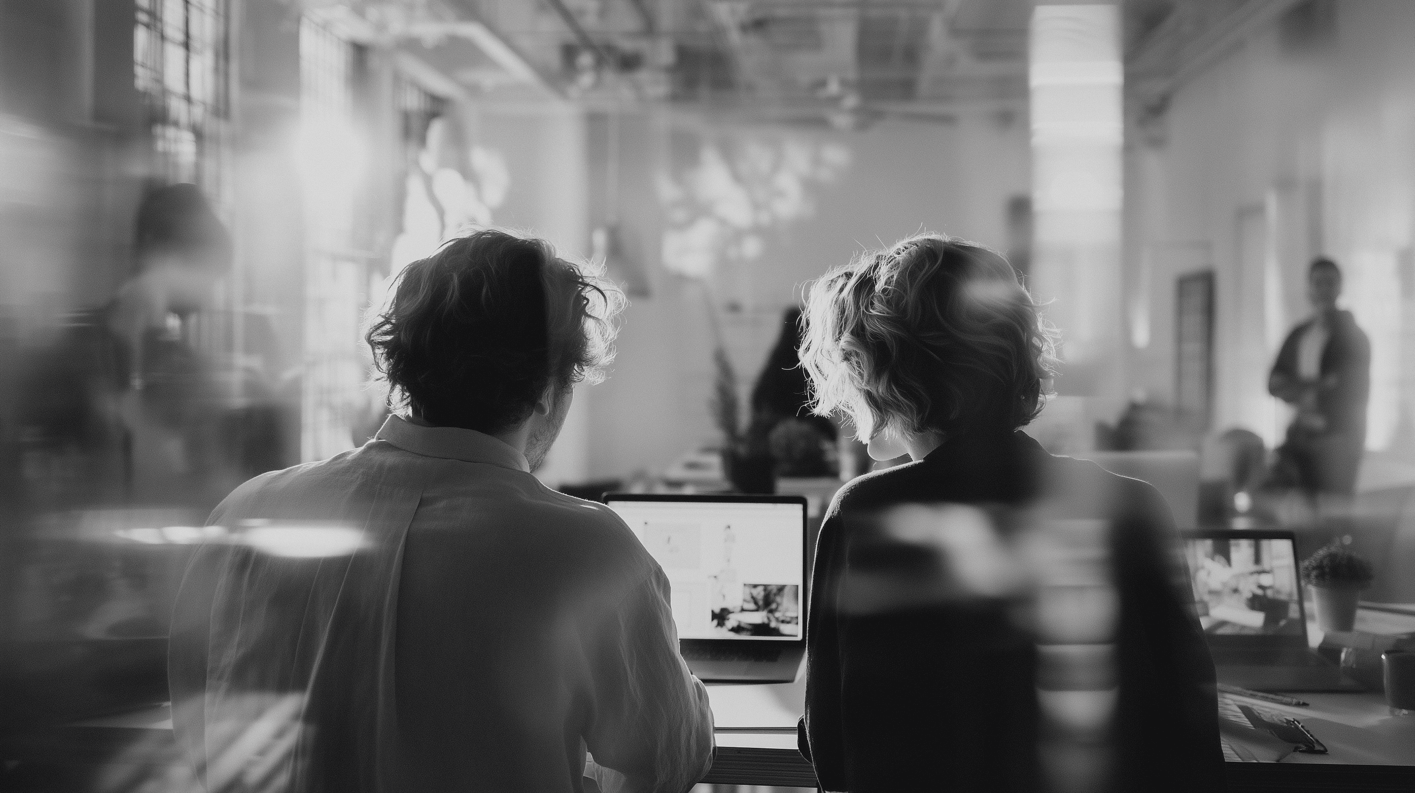Black and white image of people working at a table with laptops, showing hands gesturing during discussion of digital content displayed on screens, with fabrica® logo in the corner.
