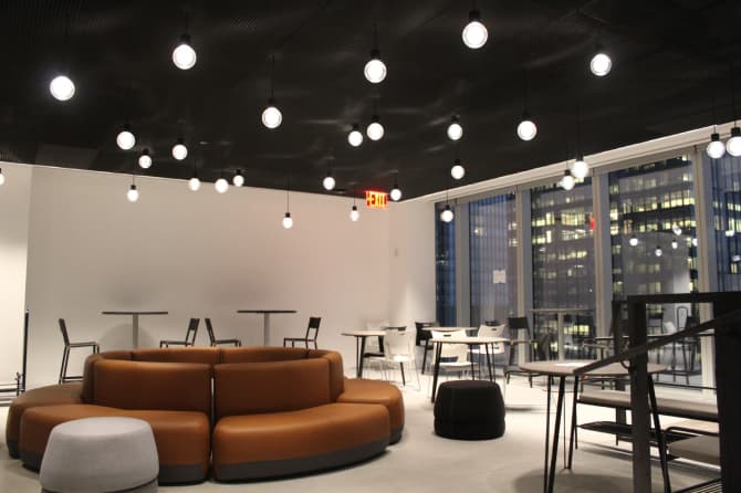 An office with a circular orange couch, big window, and hanging lights
