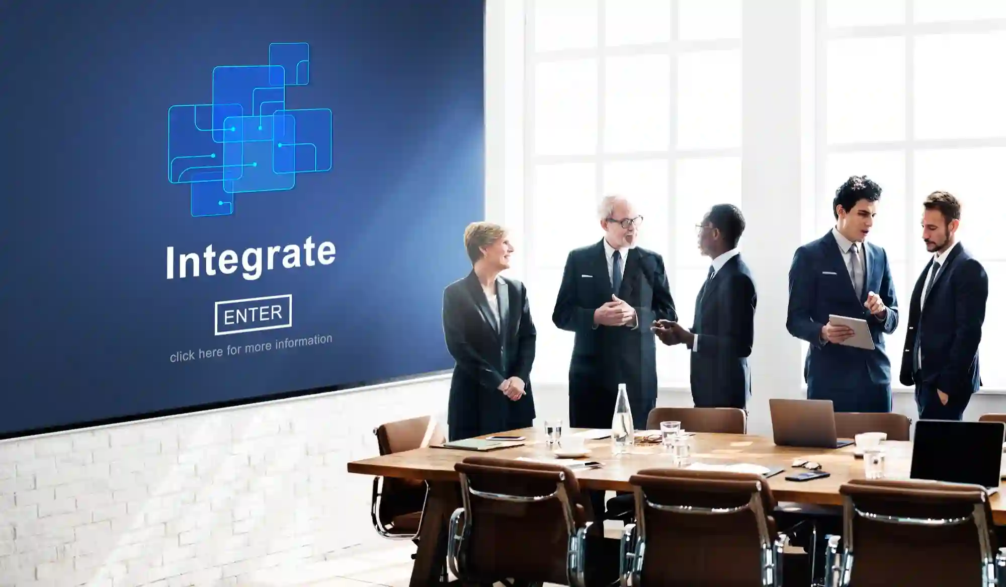 A group of professionals collaborating in a modern conference room next to a digital display featuring the word Integrate.
