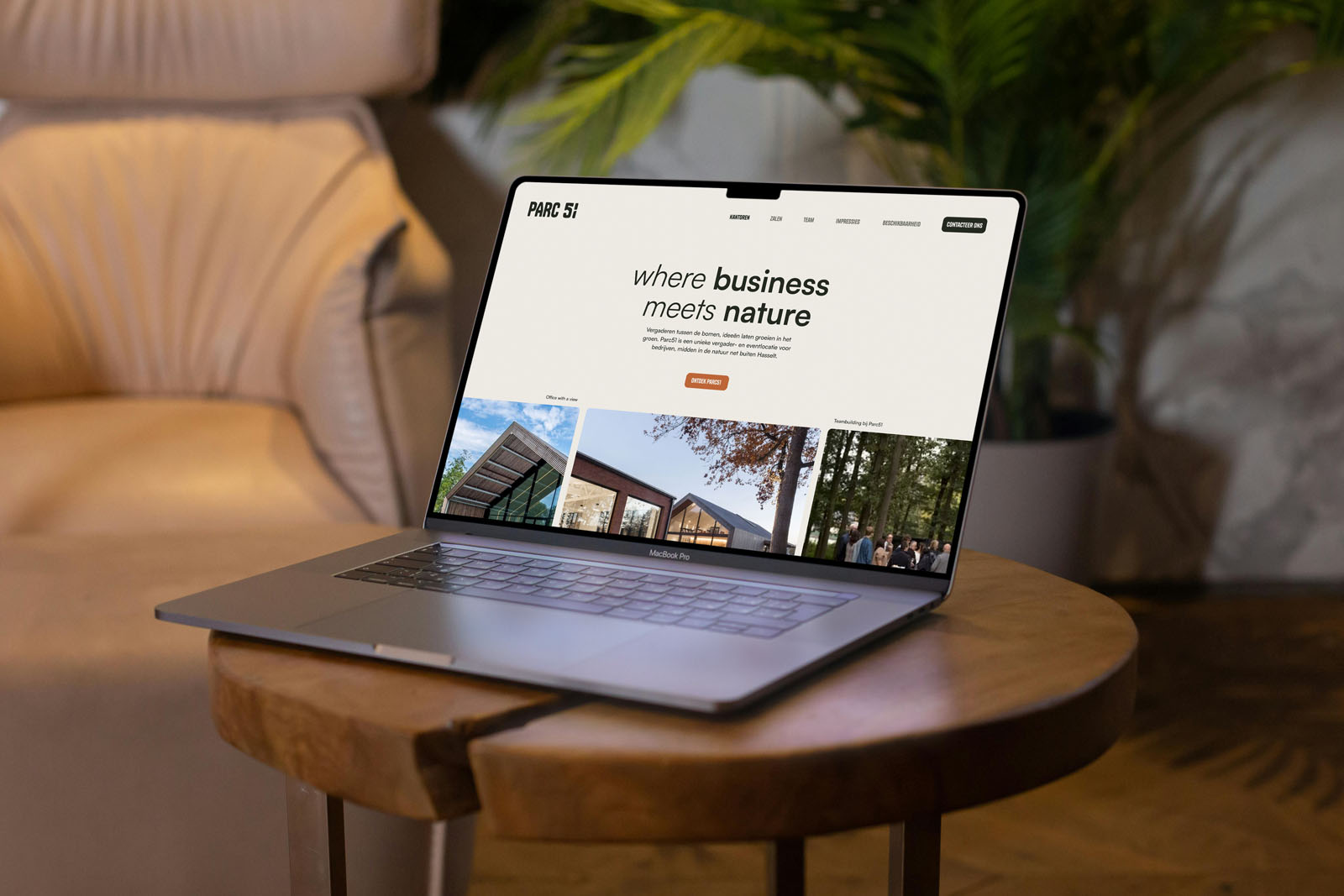 Een MacBook Pro op een houten bijzettafeltje in een warm verlicht interieur. Op het scherm is de homepage van de website van Parc51 te zien met de titel "where business meets nature".