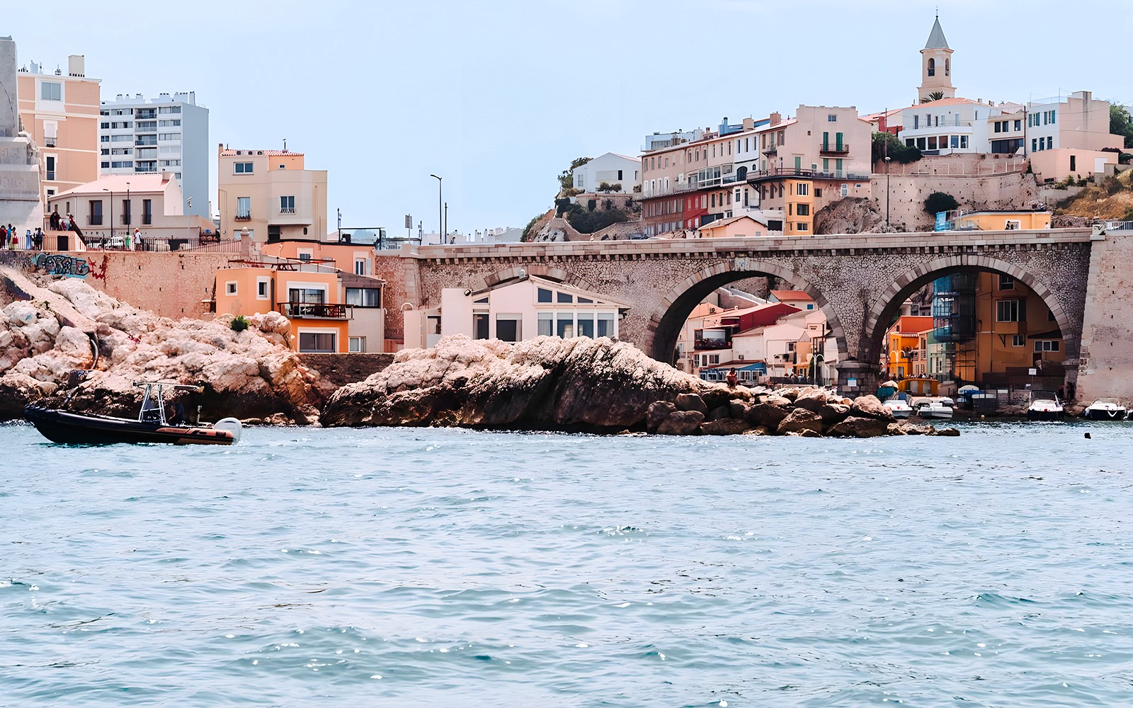 Boat near rocky shore and arched bridge in Marseille, France.