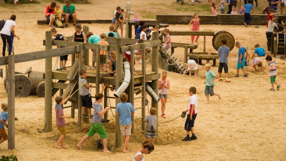 Wooden playground structures in sandy area with visitors playing