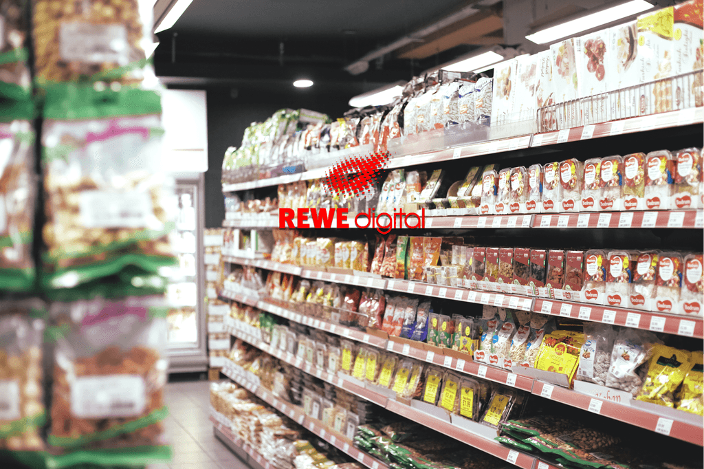 Ein sauber eingeräumtes Regal mit Gewürzen in einem Supermarkt, daruaf befindet sich das Rewe digital Logo