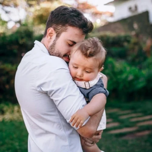 Father embracing his toddler son outdoors in a garden setting, illustrating post-procedure recovery care in Coburg, Melbourne.