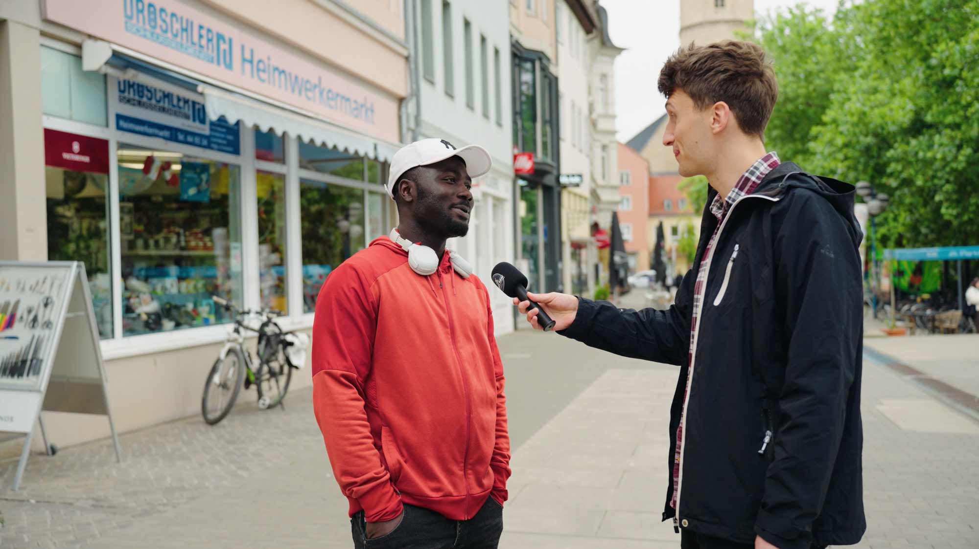 Interviewer engages with man for a strategic film production campaign ad on street, capturing storytelling for social media.