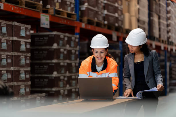 image of two people wearing hard hats in a warehouse with pallets of goods stacked up behind them