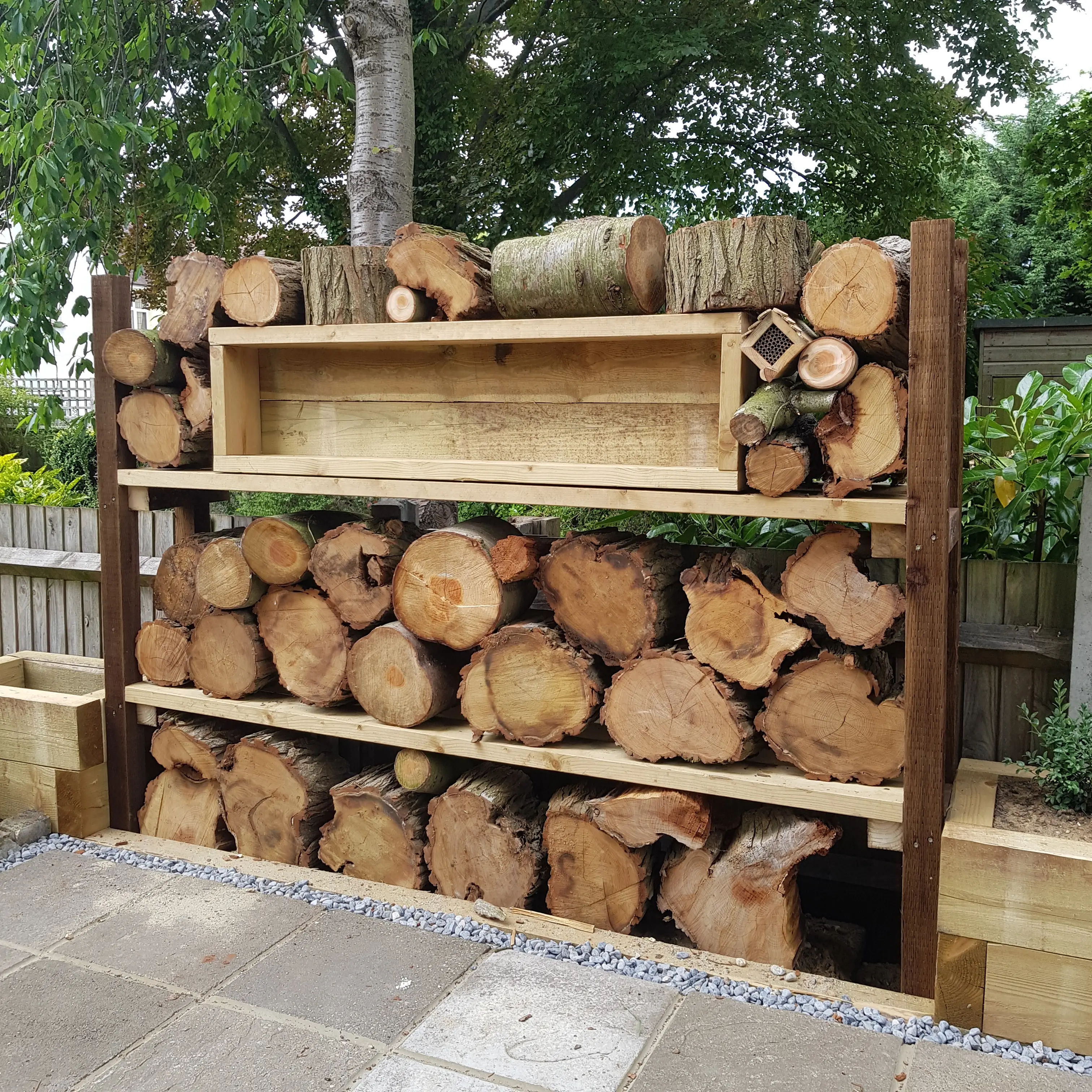 Wooden log storage featuring multiple levels of neatly stacked firewood against a natural backdrop.
