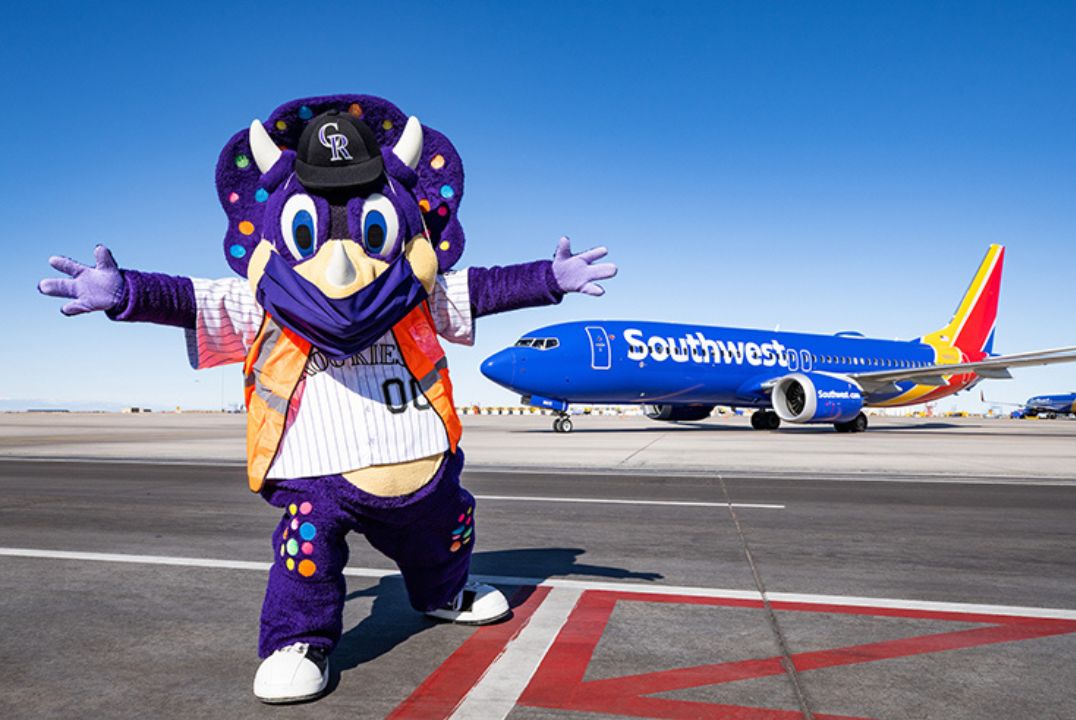 A mascot with a friendly gesture stands on the tarmac, with a Southwest Airlines plane in the backdrop, illustrating the airline's engaging brand spirit.