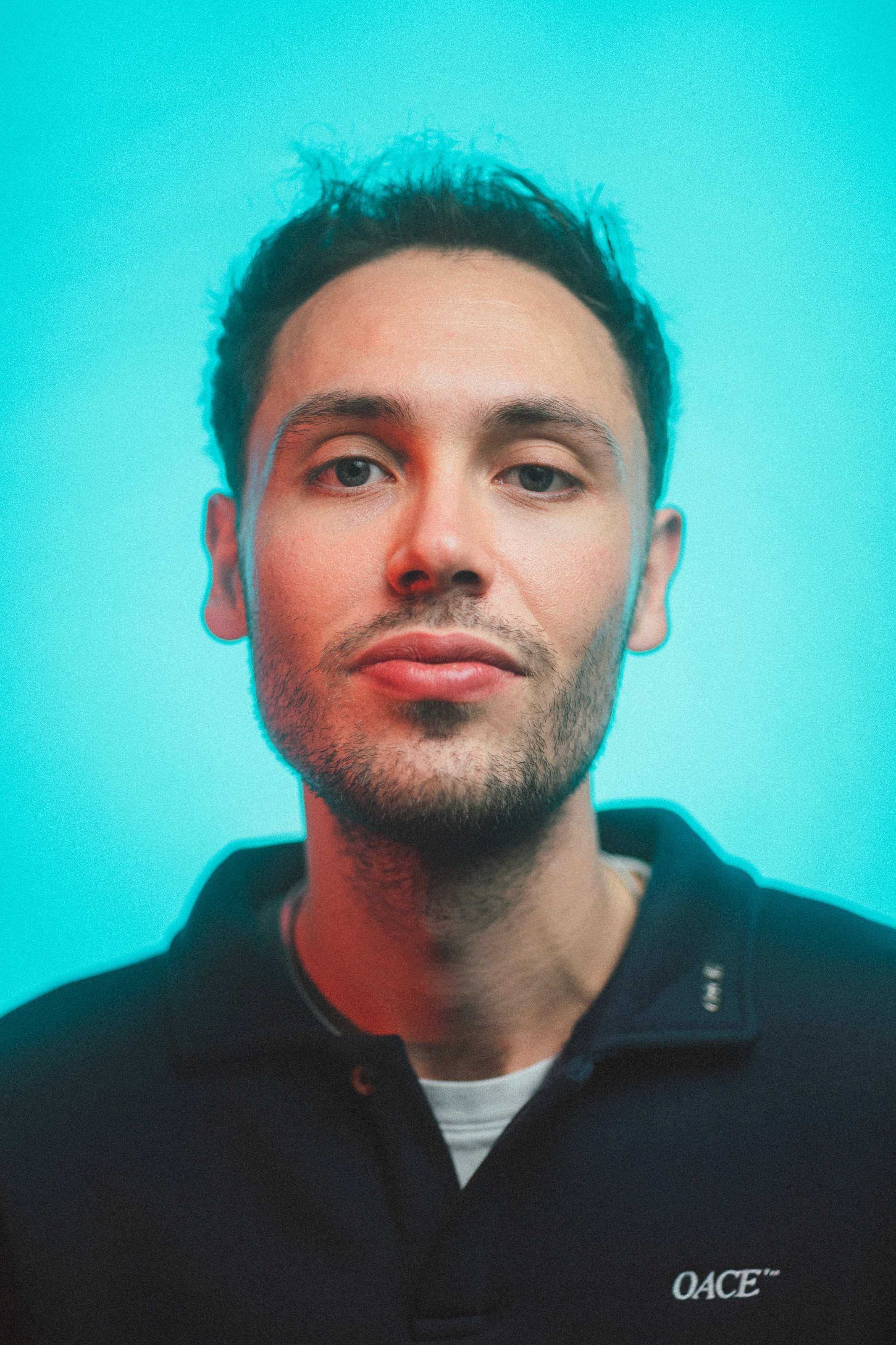 A woman with short curly hair wearing a black t-shirt looks into the camera.