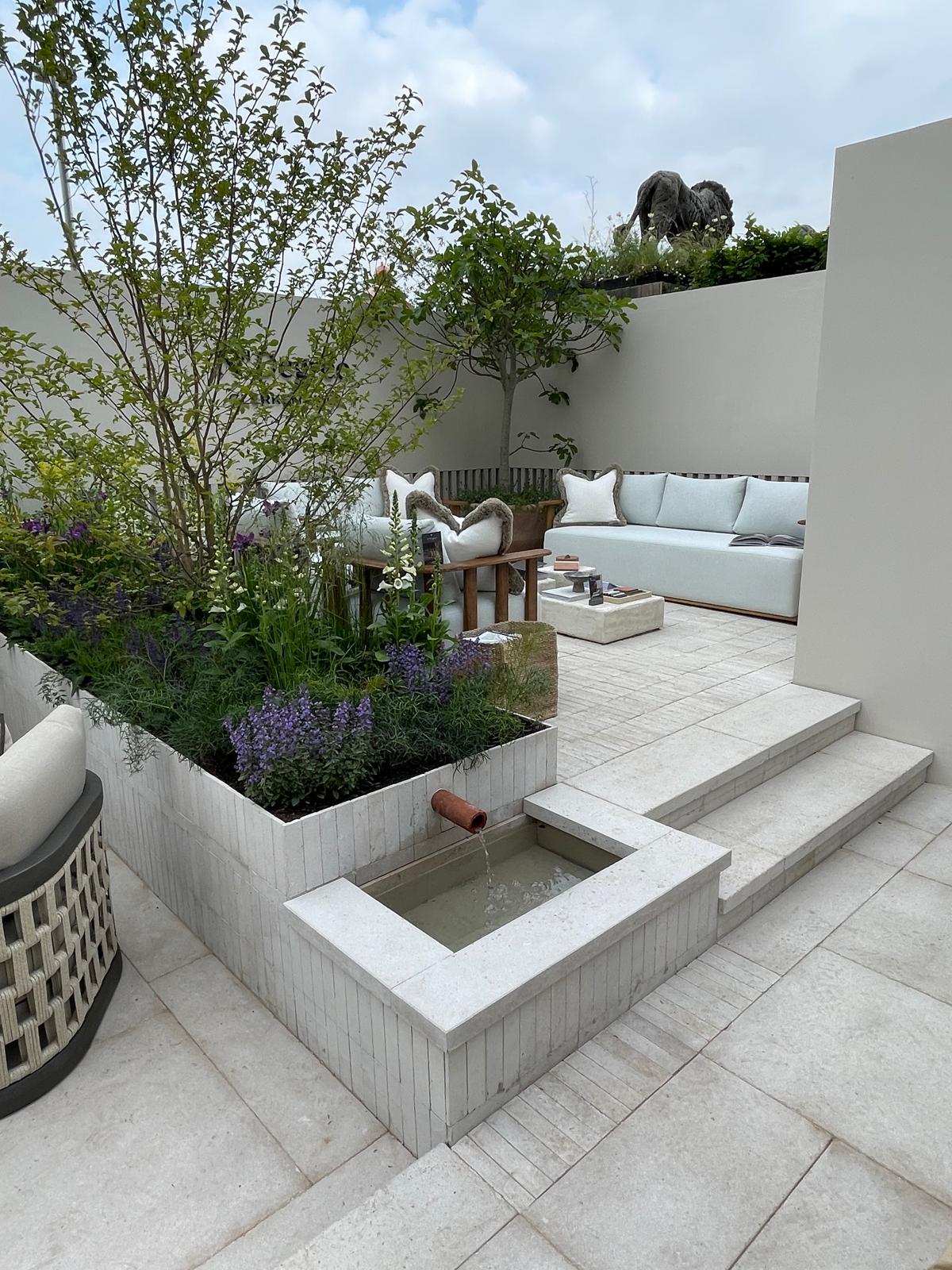 A modern outdoor space featuring a stone planter with greenery, steps leading up, and a light gray paved floor.