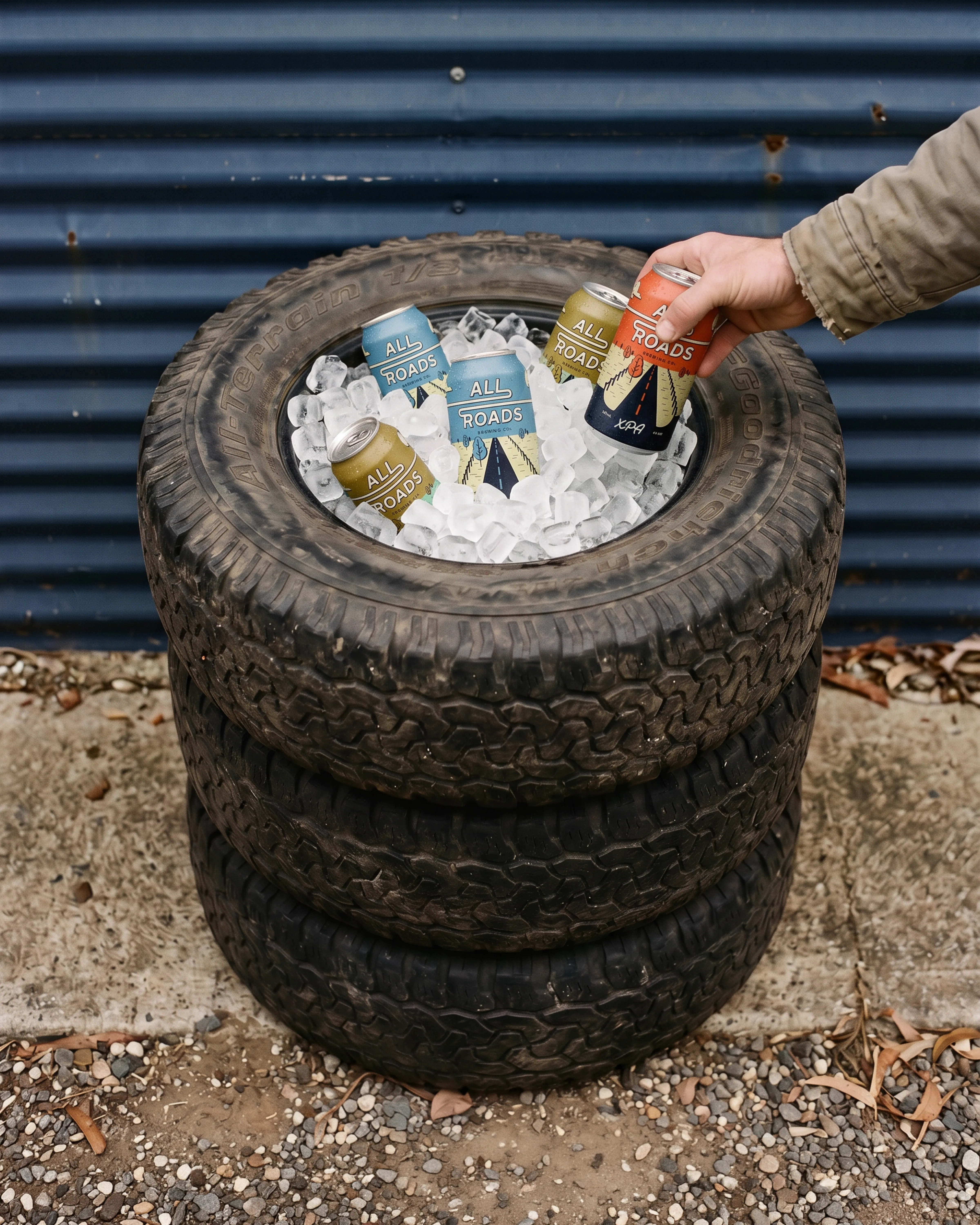 A hand reaching for an All Roads Brewing Co. can in an ice-filled tyre cooler