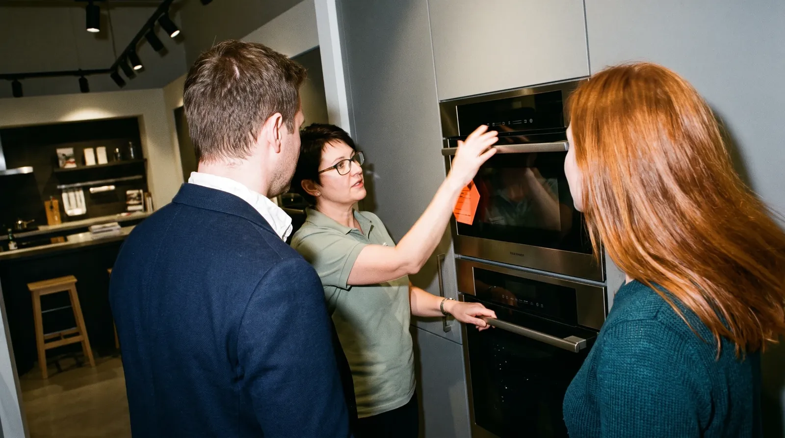 A salesperson showing a couple a wall oven in an appliance showroom