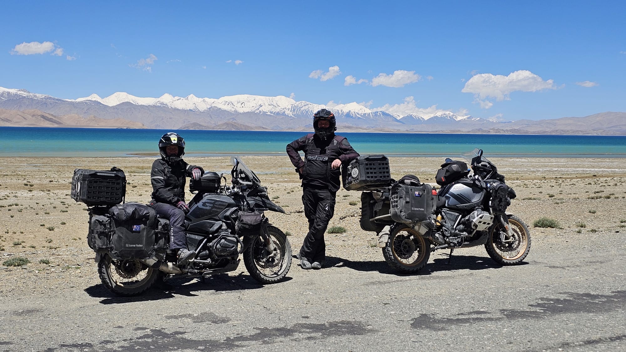 Matt and Jamie with their motorcycles beside a mountain lake.