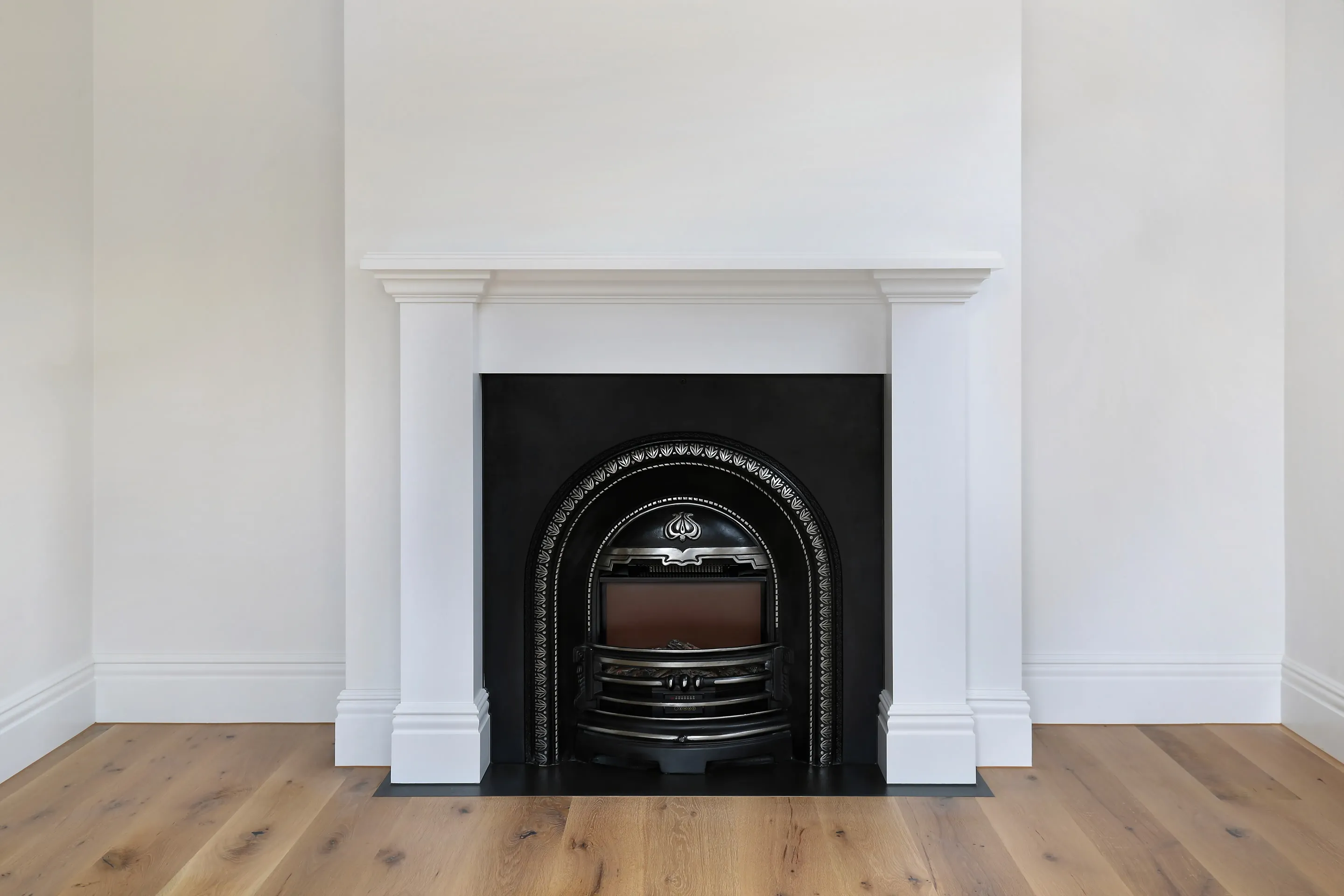 Living room feature fireplace with a white classical timber mantel, an ornate cast-iron arched insert and oak floors against white walls