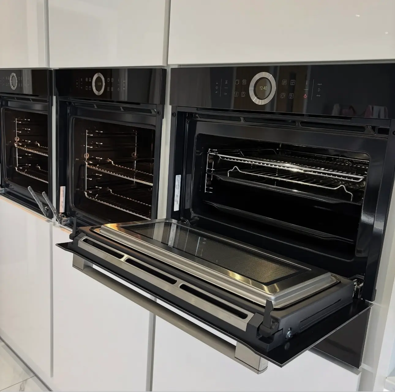 A row of built-in luxury ovens with open doors, highlighting sanitized interiors and streak-free glass as part of a post-construction appliance deep clean.