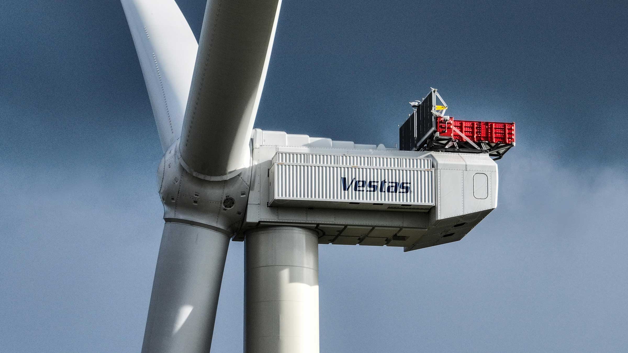 Close-up of a wind turbine nacelle with external access platform against the sky.