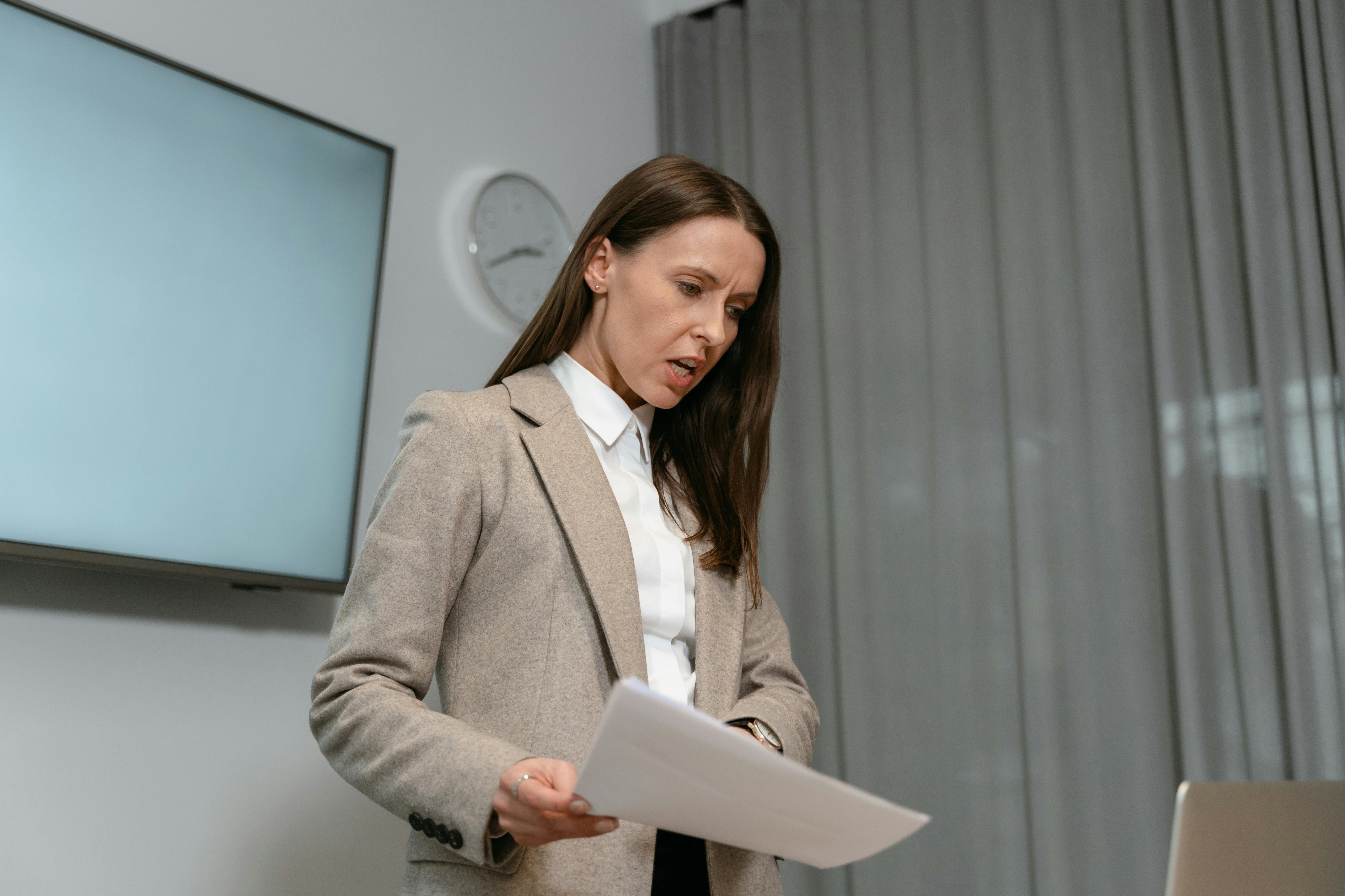 Professionista che presenta o rivede documenti in ufficio, con espressione concentrata e schermo alle spalle.