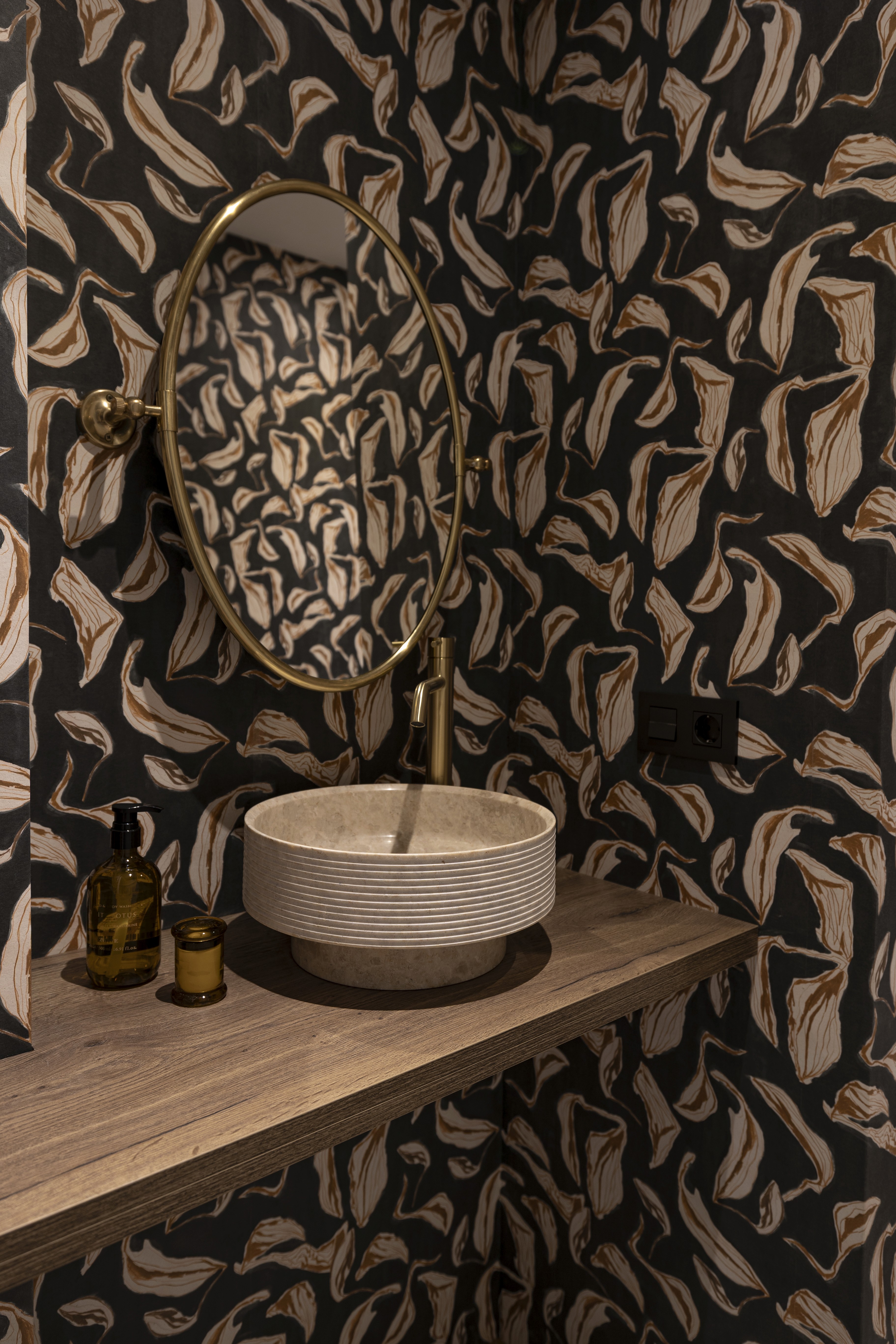 Aseo con papel pintado oscuro estampado, lavabo de piedra sobre encimera de madera y espejo ovalado