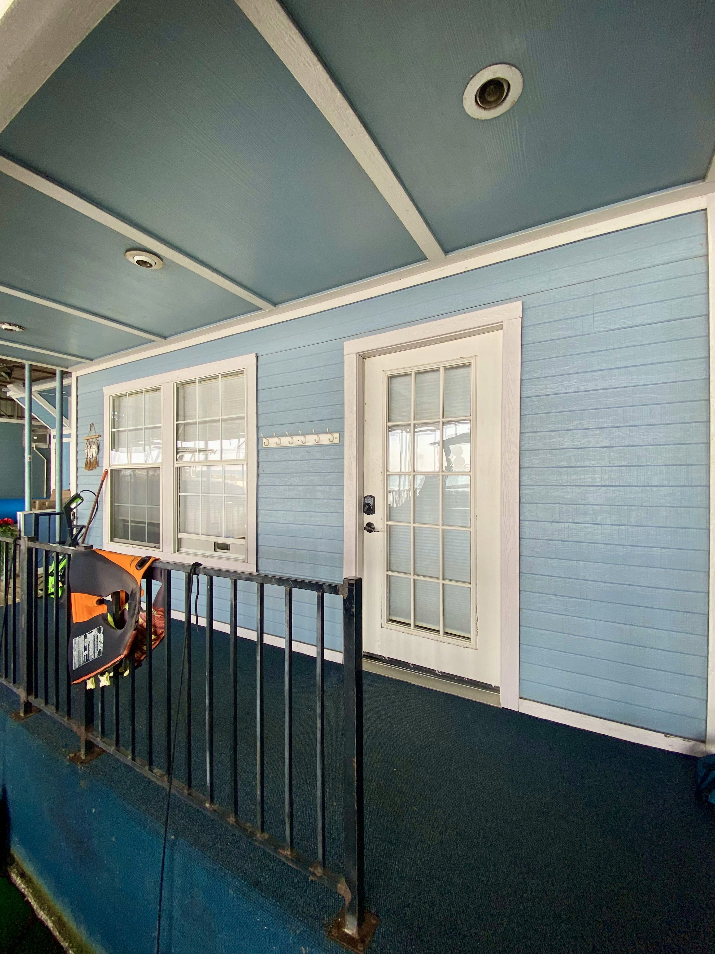 Blue porch with white door, windows, and black railing. Porch leads to an interior space. 