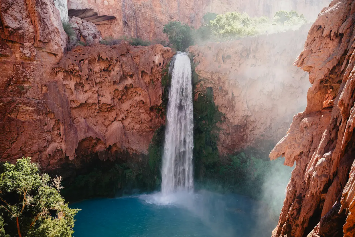 Waterfall over a blue lagoon surrounded by orange rock formations