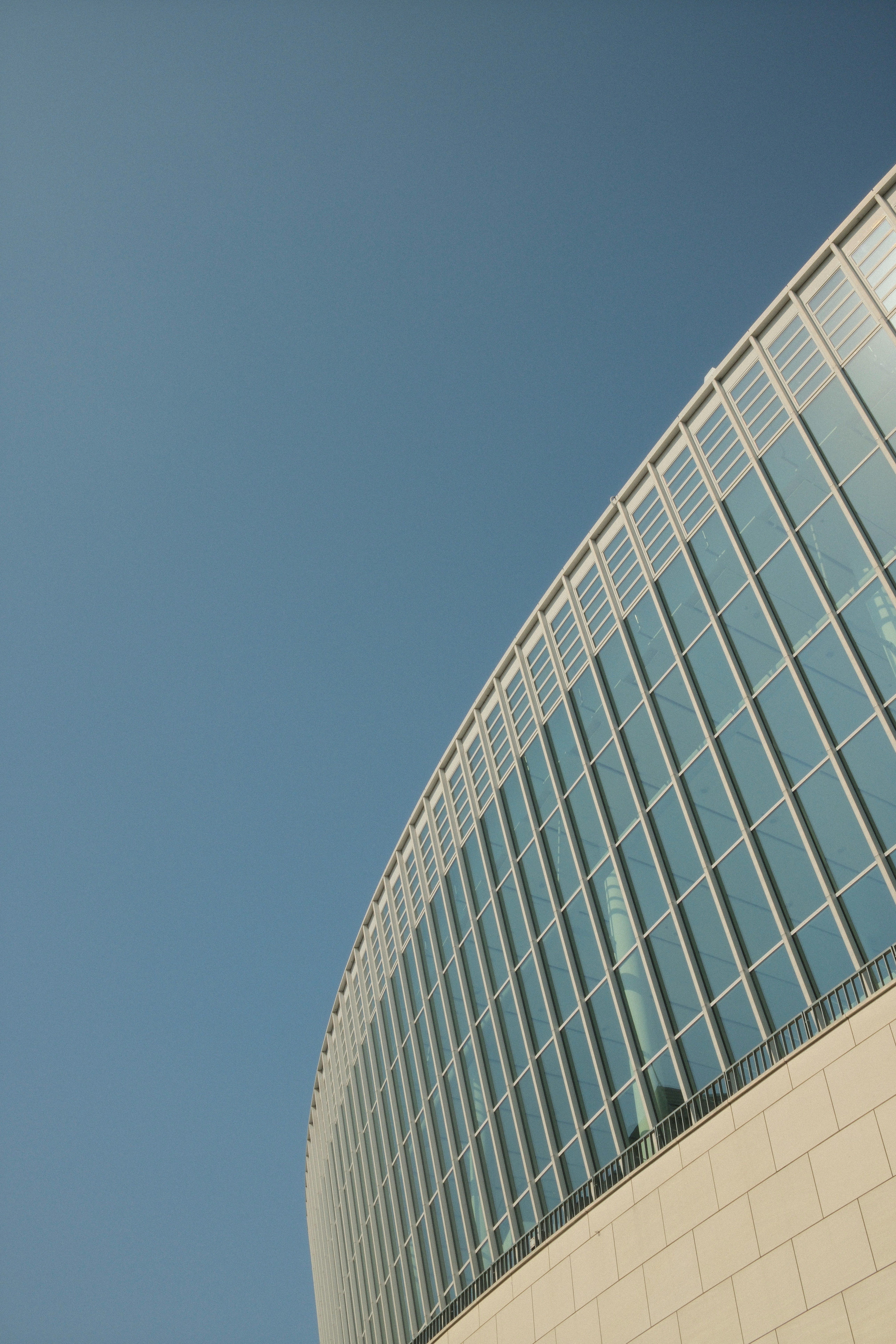 A curved glass facade of a modern building against a clear blue sky