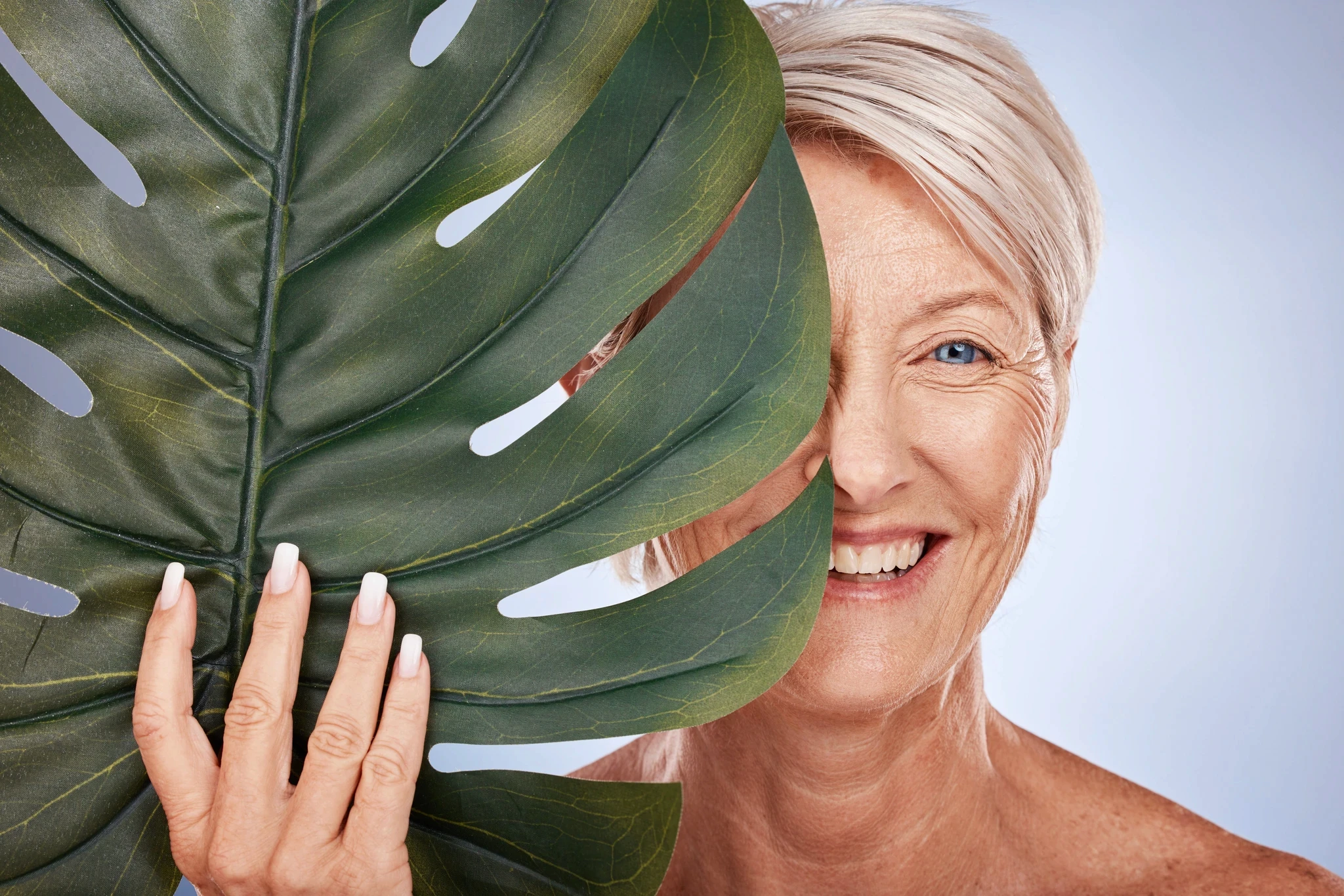 Smiling older woman partially hidden behind a large green leaf.