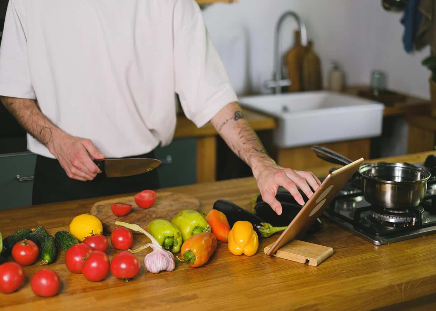 Man holding knife with veggies in front of him touching a tablet in front of him