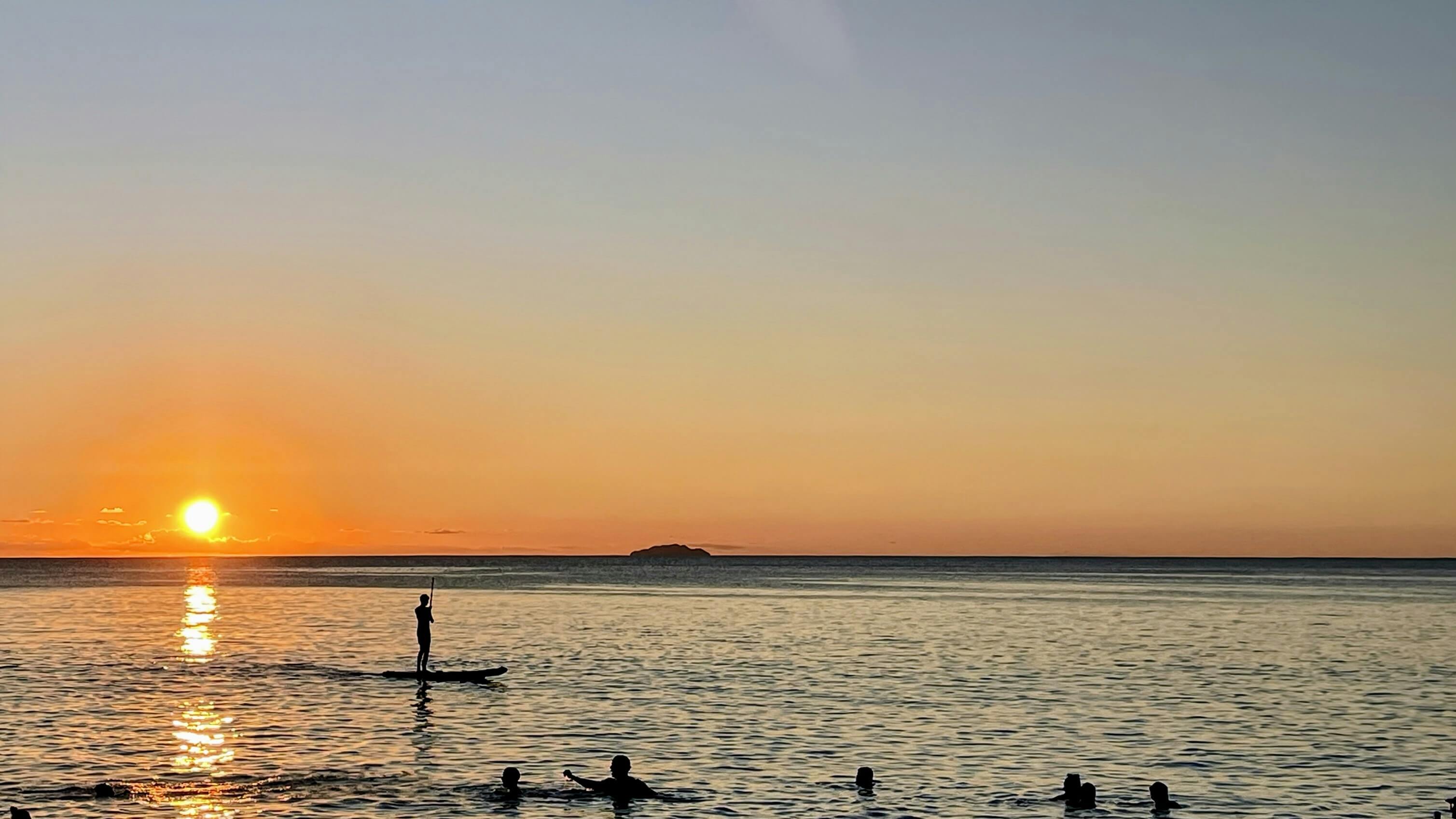 Sunset over the calm Caribbean waters in Vieques, Puerto Rico, with paddleboarders and swimmers enjoying the serene ocean view.