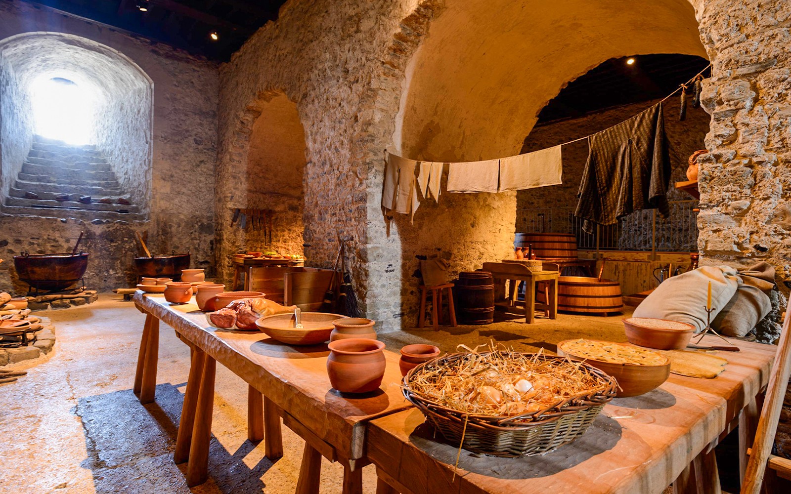 המטבח הפנימי של טירת דובר עם קירות אבן, שולחנות עץ וכלי בישול מימי הביניים.