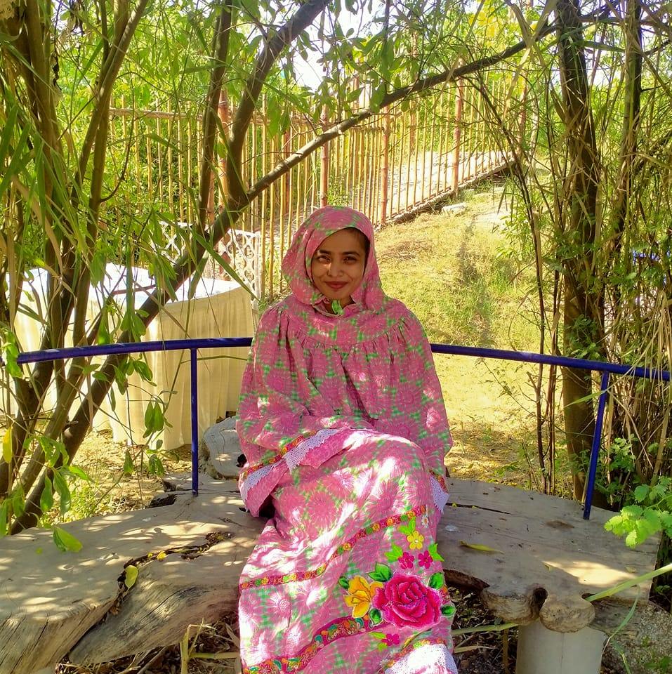 picture of team member luluwa lokhandwala, smiling and looking at the camera in a pink dress, within a lush green park space