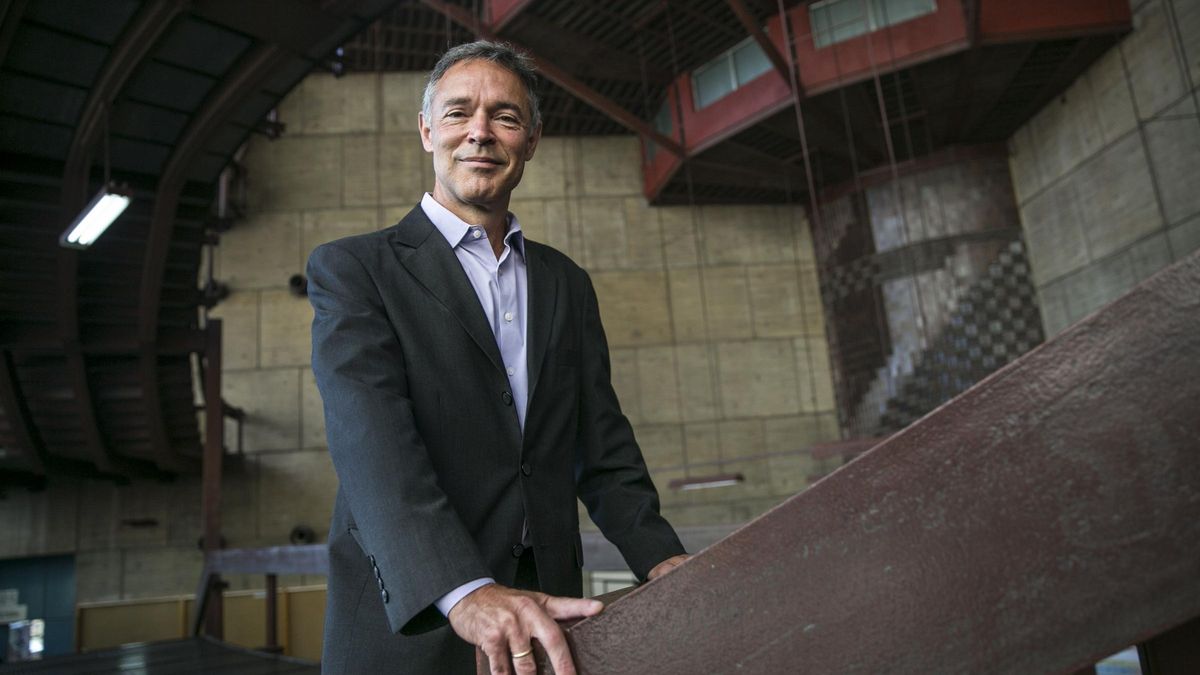 Mature man with glasses and a trimmed beard smiling confidently, standing in warm natural light against a modern backdrop.