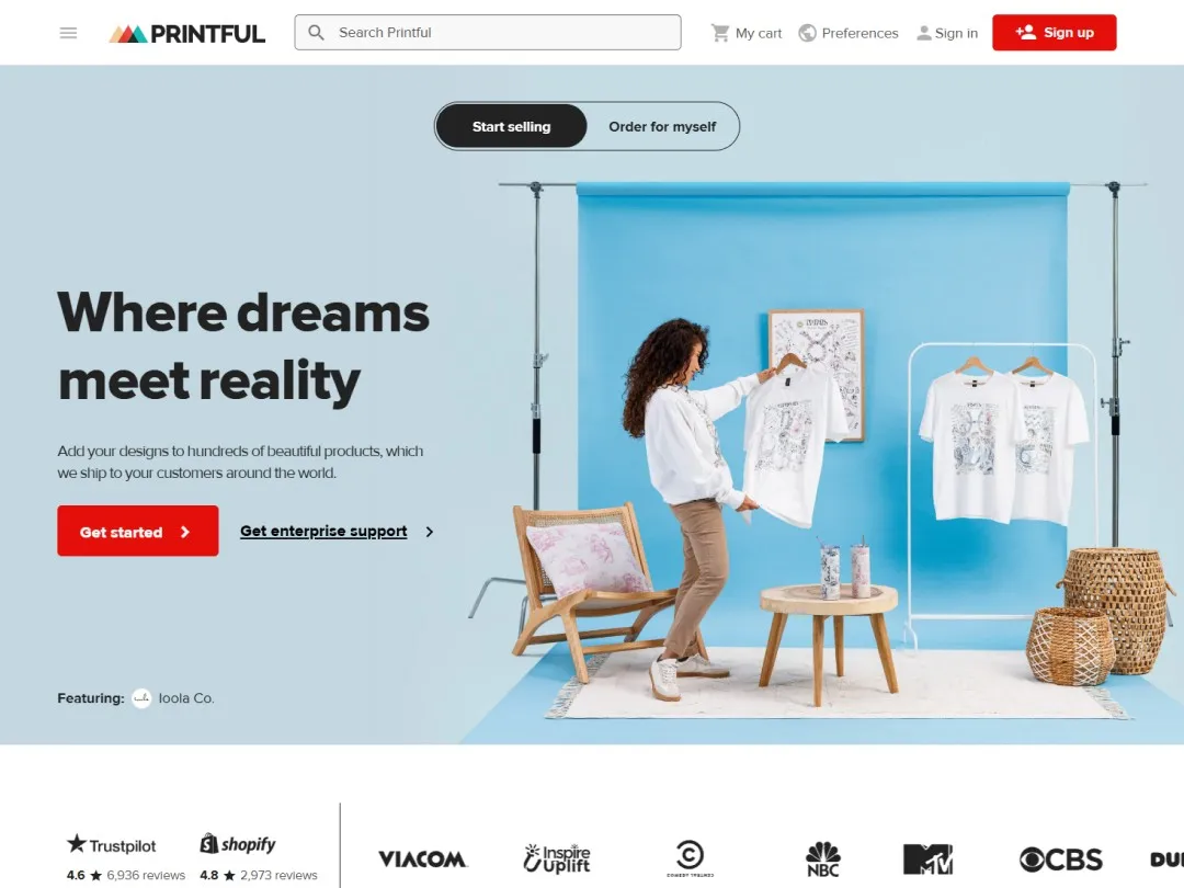 Printful website hero section with an image in the background of a woman in a photo shooting studio, looking at a t-shirt with a custom design  