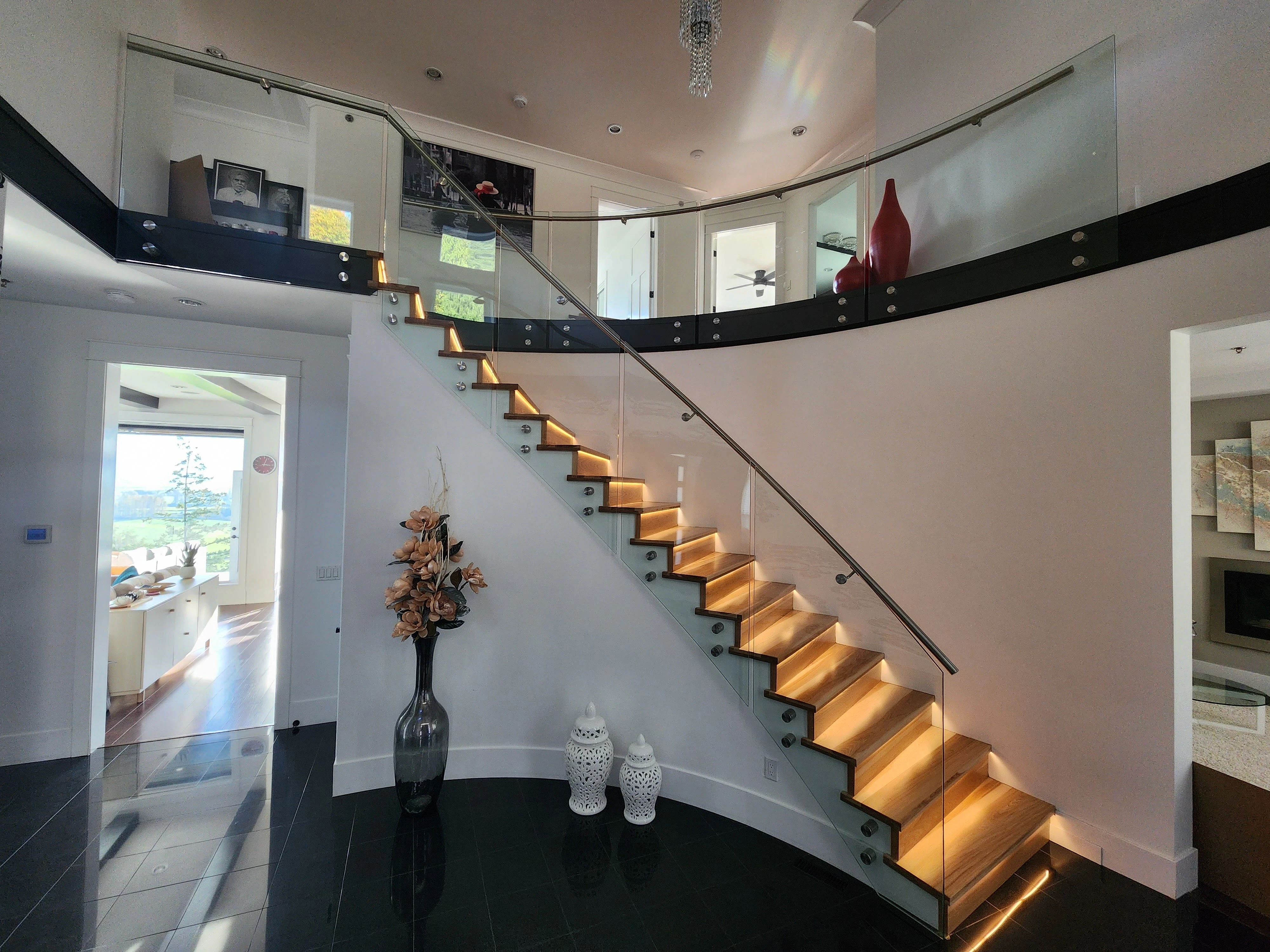 Frameless glass stair railing with round stainless standoff fixings and LED-lit wood treads in a modern home