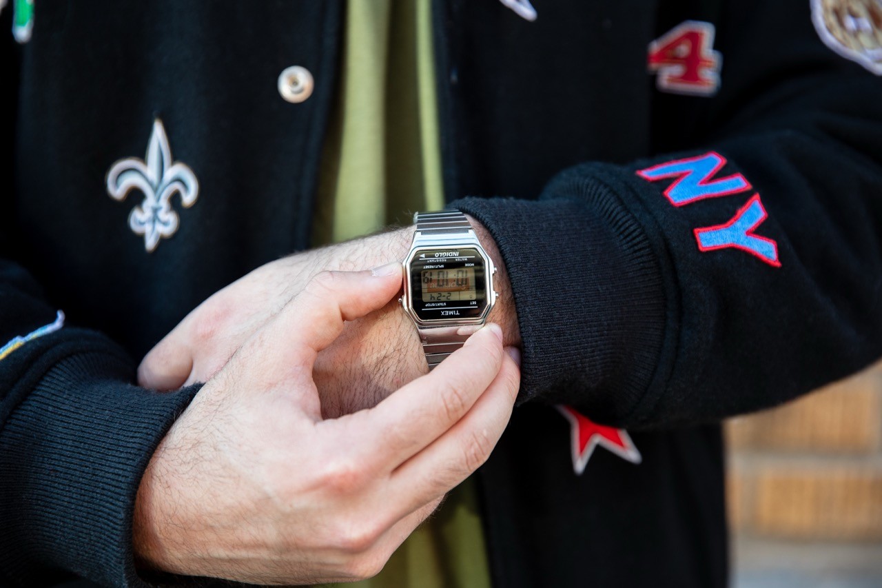Hands holding and checking a metal digital wristwatch while standing outdoors.