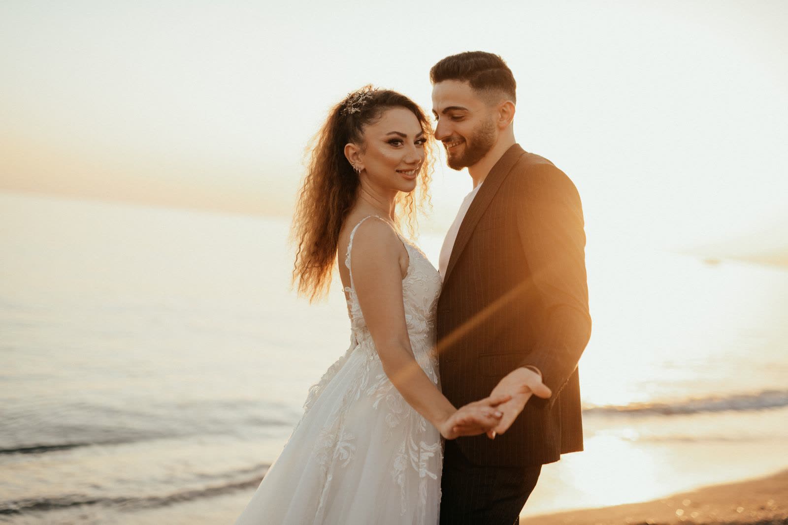 Bride and groom holding hands in front of them on a beach at sunset