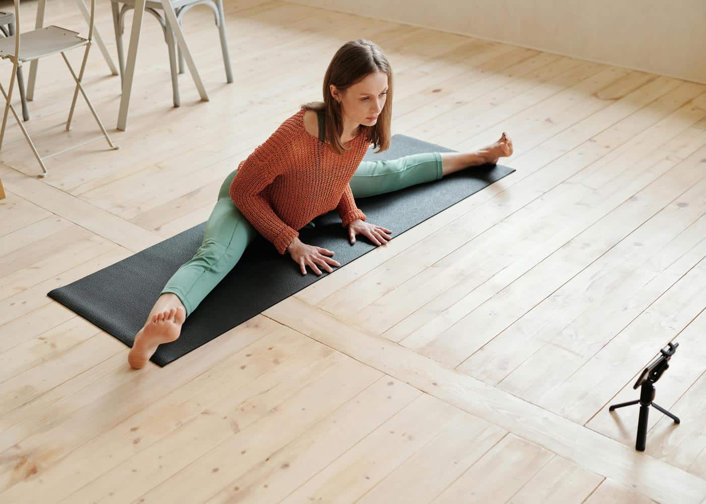Woman stretching on yoga mat while staring at phone in front of her