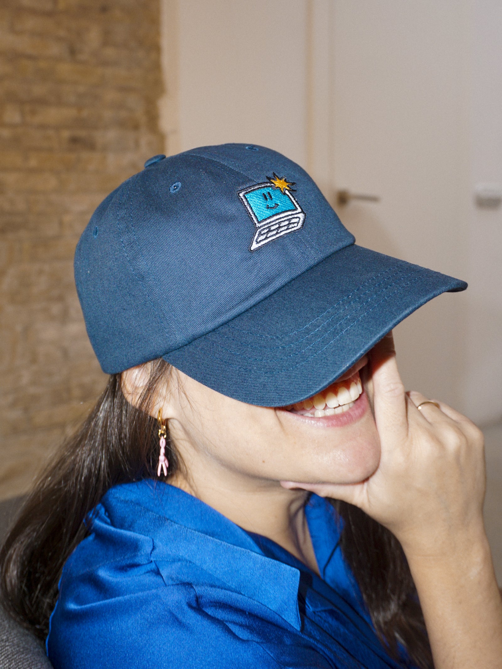 Person wearing a blue cap with a logo, smiling indoors.