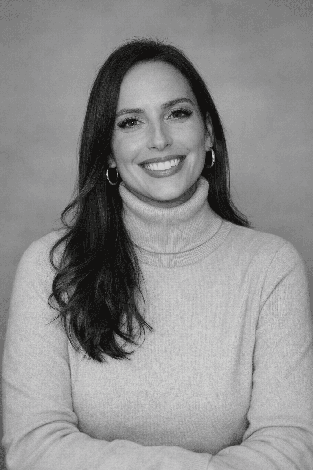 Woman in sunglasses and a brown coat stands against a vibrant blue wall. Sunlight casts a dramatic shadow, creating a confident, stylish atmosphere.