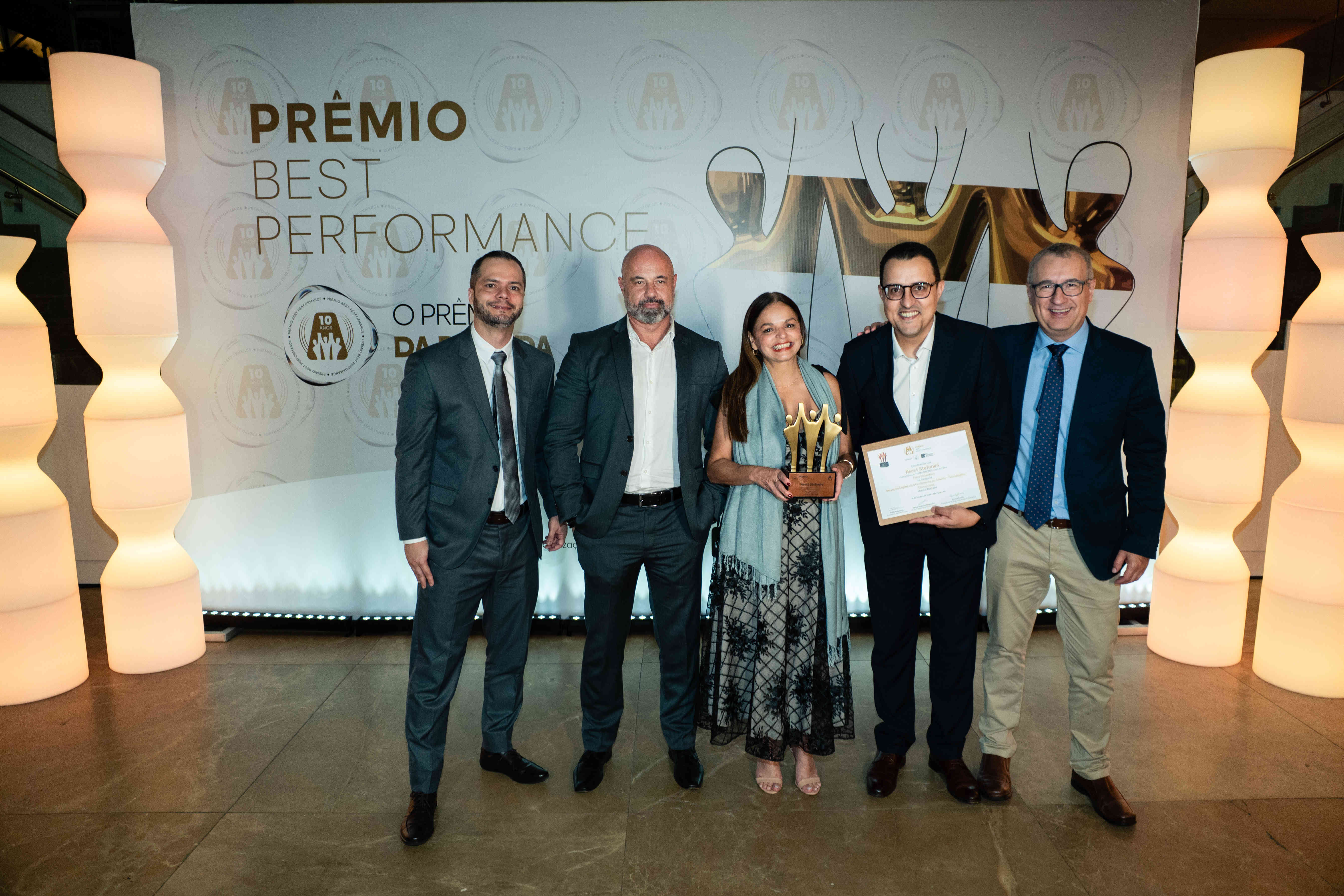 Executivos da Necxt Stefanini posando com troféu bronze e certificado no palco do Prêmio Best Performance 2025